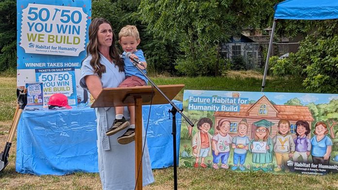 Peterborough MP Emma Harrison, with one of her children, addresses attendees at a ground-breaking ceremony on July 9, 2025 for an accessible duplex to be built on Sophia Street in Peterborough East City for seven adult women with developmental disabilities. (Photo: Bruce Head / kawarthaNOW)