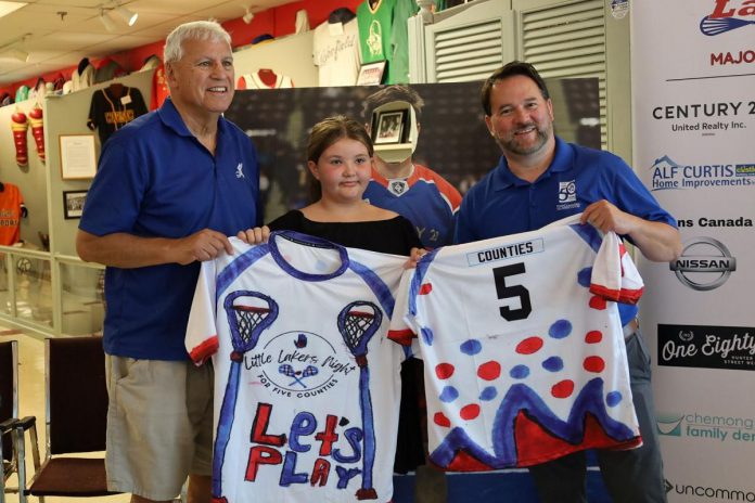 A fundraiser for Five Counties Children's Centre, Little Lakers Night returns to the Peterborough Memorial Centre on July 24, 2025 when the Peterborough Century 21 Lakers take on the Brampton Excelsiors in their final home game of the regular Major Series Lacrosse season. Pictured during a media event on July 15 are Lakers board chair Len Powers (left) and Five Counties CEO Scott Pepin (right) with nine-year-old Kennedy Meredith, who designed the special jersey that Lakers players will wear during the pre-game warmup before being auction off in support of Five Counties. (Photo: Peterborough Century 21 Lakers) A fundraiser for Five Counties Children's Centre, Little Lakers Night returns to the Peterborough Memorial Centre on July 24, 2025 when the Peterborough Century 21 Lakers take on the Brampton Excelsiors in their final home game of the regular Major Series Lacrosse season. Pictured during a media event on July 15 are Lakers board chair Len Powers (left) and Five Counties CEO Scott Pepin (right) with nine-year-old Kennedy Meredith, who designed the special jersey that Lakers players will wear during the pre-game warmup before being auction off in support of Five Counties. (Photo: Peterborough Century 21 Lakers)