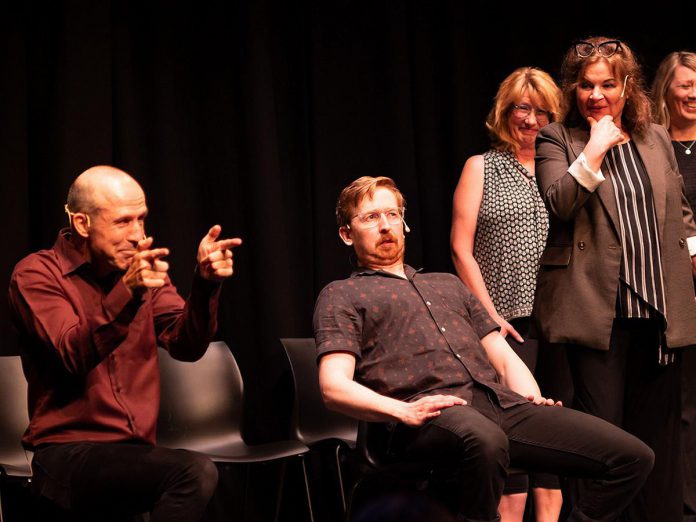 Kerry Griffin (left) performs an unconventional kind of therapy on Mark Rostrup as Janet Van Der Graaff, Linda Kash, and Naomi Snieckus look on during klusterfork's "School's Out!" improv show at the Market Hall in July 2023. (Photo: Andy Carroll)
