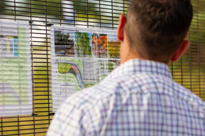 An attendee during an event on August 6, 2025 to celebrate the opening of the donor-funded Psychiatric Intensive Care Unit (PICU) courtyard at Peterborough Regional Health Centre (PRHC) looks at renderings for the second phase of the courtyard, which will see additional landscaping including a rock wall and gardens. (Photo: Jordan Lyall Photography for kawarthaNOW)