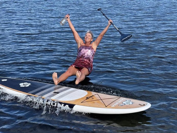 Tanya Rightmyer jumps off her stand-up paddleboard on August 24, 2025 to celebrate completing her personal challenge of paddling along the entire shoreline and around each island with a cottage on it on Chandos Lake. It was an opportunity to chat with cottagers on the lake, see wildlife, and raise awareness about how clean the lake is. (Photo via Tania Rightmyer / Facebook)