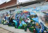 This summer, more than 70 Bancroft and area professional and amateur artists helped revitalize an iconic mural on the west side of the 23 Bridge Street building as part of the "Embrace" community-driven project held by A Place for the Arts. The revitalized mural, which was originally painted by celebrated local artist Arne Roosman in 2014, was unveiled at a celebratory community event on September 13, 2025. (Photo: Megan Gallant / kawarthaNOW)