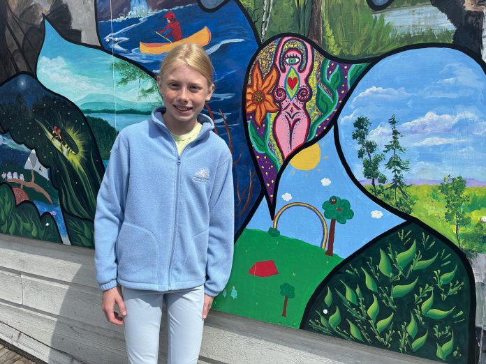 11-year-old Amelia Taylor was among the more than 70 Bancroft and area artists, both amateur and professional, who painted a segment to revitalize a mural on the west side of the 23 Bridge Street building in Bancroft. To showcase some of her favourite things about Bancroft, Taylor painted a rainbow shining over a campsite as turtles walked by. (Photo: Megan Gallant / kawarthaNOW)