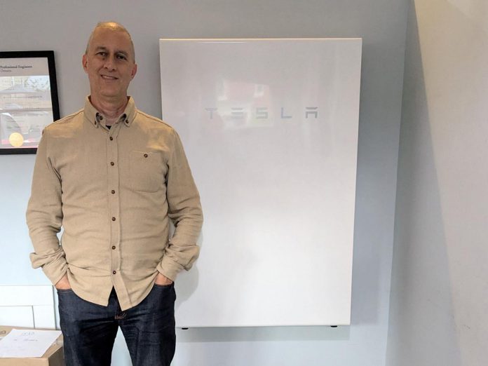 Generation Solar co-owner and vice-president JP Pawliw poses with a Tesla Powerwall, one of two backup batteries installed in their offices. This battery is not connected to a solar system but still provides backup power during outages. (Photo: Clara Blakelock / GreenUP)