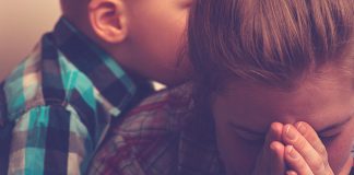 Peterborough parents feel isolated and overwhelmed, according to new research report A women covers her face with her hands with a young boy in the background. (Stock photo)