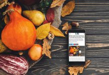 A smartphone sitting on a harvest table covered with squash and fall leaves displaying kawarthaNOW's Thanksgiving Monday 2025 holiday hours story. (kawarthaNOW photo)