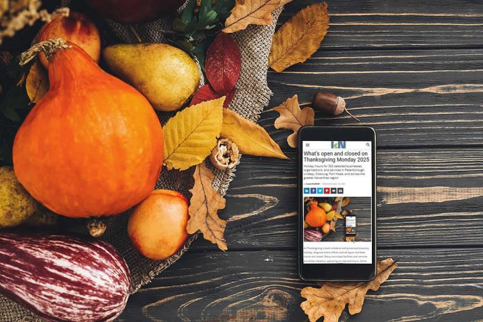 A smartphone sitting on a harvest table covered with squash and fall leaves displaying kawarthaNOW's Thanksgiving Monday 2025 holiday hours story. (kawarthaNOW photo)