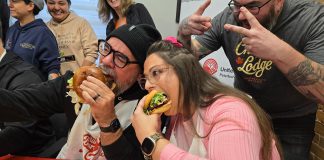 "Burger ambassadors" Jason Wilkins and Tiffany Arcari sink their teeth into burger creations from Double Dz's and Chemong Lodge (with Chemong Lodge's sous chef Sean Crooks giving the victory sign) during the launch of the United Way Peterborough & District's inaugural Ultimate Burger Battle community fundraiser on October 30, 2025 at the United Way office. During the month of November, eight participating restaurants will be creating a unique and creative burger in a friendly competition for the title of Ultimate Burger of the Year, with $2 from every burger sold being donated to the United Way. (Photo: Jeannine Taylor / kawarthaNOW)
