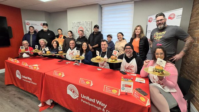 At a media event on October 30, 2025, representives from the eight restaurants in the city and county of Peterborough that are participating in the United Way Peterborough & District's inaugural Ultimate Burger Battle community fundraiser stand behind the eight "burger ambassadors" (Paul Rellinger, Laura Montague, Dan O'Toole, Neil Morton, Nour Mazloum, Pete Dalliday, Jason Wilkins, and Tiffany Arcari) who will be promoting the November event. Along with awards for the Ultimate Burger of the Year and Most Burgers Sold, the fundraiser will include the People's Choice Awards, whose winners will be selected by community members voting online for their favourite burger. (Photo: Jeannine Taylor / kawarthaNOW)