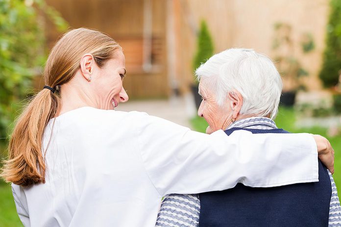 A young woman with her arm around the shoulders of an elderly person. (Stock photo)