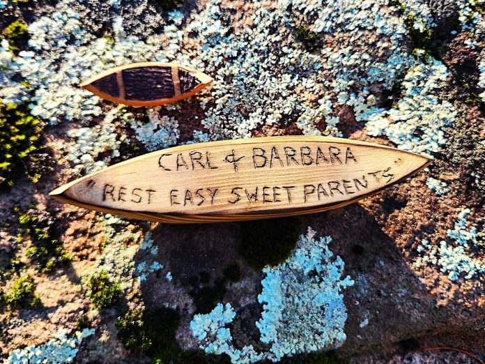 One of artist Daniel Marlatt's six-inch canoes to be released into the Miskwaa Ziibi river in spring 2026 as part of the "Dedicate a Canoe" social project. Above the dedication canoe is one of the canoes from Marlatt's "lil Red Canoe" project, which inspired his latest project. There is no cost to participate in Marlatt's "Dedicate a Canoe" project, with the only obligation to visit Miskwaa Art Studio and Outdoor Gallery in the spring to release the canoe into the Miskwaa Ziibi river. (Photo courtesy of Daniel Marlatt)