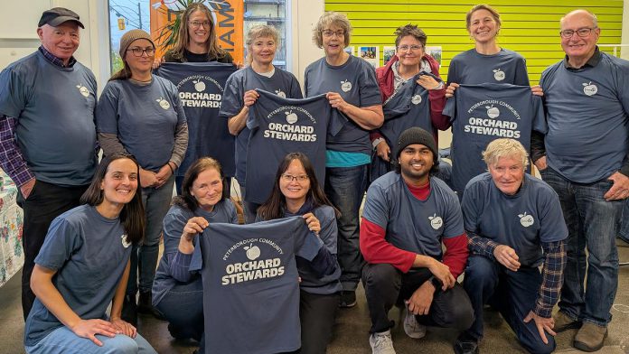 The Peterborough Community Orchard Stewards recently gathered at the GreenUP office for an end-of-season lunch. Pictured here taking a break from reflection and goal setting to show off their newly printed T-shirts, the group tends to 13 fruit orchards planted in neighbourhoods around Peterborough. (Photo: Tegan Moss / GreenUP)