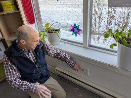 GreenUP energy advisor Bryn Magee points to an electrical outlet on an exterior wall in the GreenUP office. In many older buildings, electrical outlets are sources of air leakage. Foam gaskets and plug protectors can help to staunch the flow of cold air. (Photo: Clara Blakelock / GreenUP)