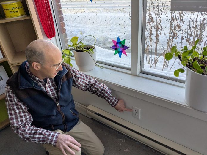GreenUP energy advisor Bryn Magee points to an electrical outlet on an exterior wall in the GreenUP office. In many older buildings, electrical outlets are sources of air leakage. Foam gaskets and plug protectors can help to staunch the flow of cold air. (Photo: Clara Blakelock / GreenUP) GreenUP energy advisor Bryn Magee points to an electrical outlet on an exterior wall in the GreenUP office. In many older buildings, electrical outlets are sources of air leakage. Foam gaskets and plug protectors can help to staunch the flow of cold air. (Photo: Clara Blakelock / GreenUP)