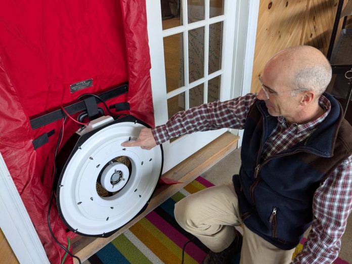 GreenUP energy advisor Bryn Magee demonstrates the setup of a blower door at the GreenUP offices. The fan is normally installed in an exterior door, where it depressurizes the home, accentuating any air leaks present in the home. Depending on how leaky the home is, an energy advisor will set up a fan using different ring sizes during a blower door test. A more airtight home will use smaller rings, while a leakier home requires more fan power and a larger ring size. (Photo: Clara Blakelock / GreenUP)