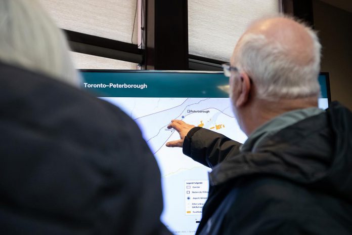 An attendee at the open house on the proposed Alto high-speed rail network between Toronto and Quebec City, held at the McDonnel Street Activity Centre in Peterborough on February 26, 2026, gestures at a map showing the corridor at Peterborough, where an Alto station will be located. (Photo: Jordan Lyall / kawarthaNOW)