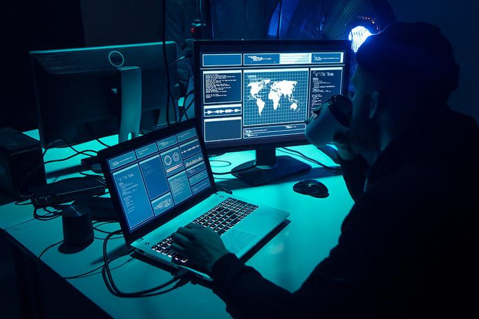 A hacker with a laptop and a secondary monitor showing data. (Stock photo)