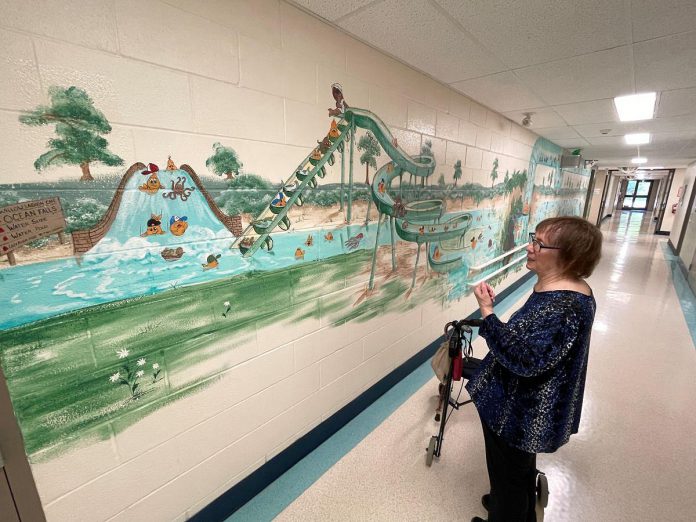 Artist Pat Calvert looks at her expansive, water-themed mural that is spread out and still graces the hallways and treatment room walls at Five Counties Children's Centre in Peterborough. Completed in 2002, the mural still holds the attention and interest of Five Counties clients and families as much today as it did 25 years ago. (Photo: Five Counties Children's Centre)