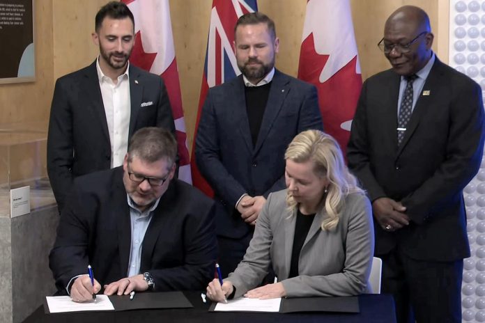 Ontario Power Generation senior vice president Paul Séguin and Port Hope mayor Olga Hankivsky sign a memorandum of understanding (MOU) at the Nuclear Discovery Centre in Port Hope on February 12, 2026 to advance what would be the world's largest nuclear power plant, located in Wesleyville. (kawarthaNOW screenshot of Ontario government video)