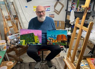 Artist David Geene in his home studio with two 12 by 16 inch paintings of existing buildings that will be featured in his "Economies of Scale?" solo exhibit at Watson & Lou in downtown Peterborough from April 4 to 25, 2026. Titled (left to right) "196 Hunter Street East" and "212 Brock Street from Hunter W. and Aylmer Streets," the works are two of the 12 acrylic paintings that aim to explore the politics and ethics of two proposed high-rise structures in Peterborough, at 90 Hunter Street and on Crescent Street. Including interpretations of the proposed buildings, the exhibit will launch with an opening reception from 2 to 4 p.m. on Saturday, April 4. (Photo courtesy of David Geene)