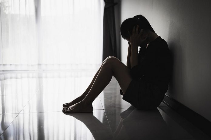 A silhouette of a distressed young woman sitting on the floor. (Stock photo)