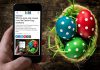 A mobile phone showing kawarthaNOW's Easter 2026 holiday hours over a table with a basket of decorated Easter eggs. (Photo: kawarthaNOW)