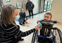Five Counties Children's Centre occupational therapist Jess hands an ornament to two-year-old Arthur during a recent treatment session. With the help of Five Counties staff, Arthur has taken a significant course correction after a rare form of childhood cancer left him paralyzed from the waist down, including with a mini stand-up wheelchair known as a mobile stander. (Photo courtesy of Five Counties Children's Centre)
