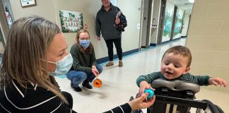 Five Counties Children's Centre occupational therapist Jess hands an ornament to two-year-old Arthur during a recent treatment session. With the help of Five Counties staff, Arthur has taken a significant course correction after a rare form of childhood cancer left him paralyzed from the waist down, including with a mini stand-up wheelchair known as a mobile stander. (Photo courtesy of Five Counties Children's Centre)