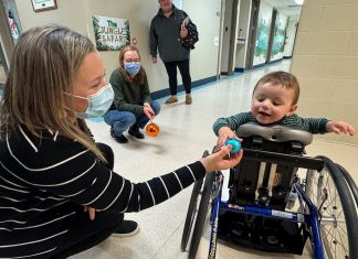 Five Counties Children's Centre occupational therapist Jess hands an ornament to two-year-old Arthur during a recent treatment session. With the help of Five Counties staff, Arthur has taken a significant course correction after a rare form of childhood cancer left him paralyzed from the waist down, including with a mini stand-up wheelchair known as a mobile stander. (Photo courtesy of Five Counties Children's Centre)