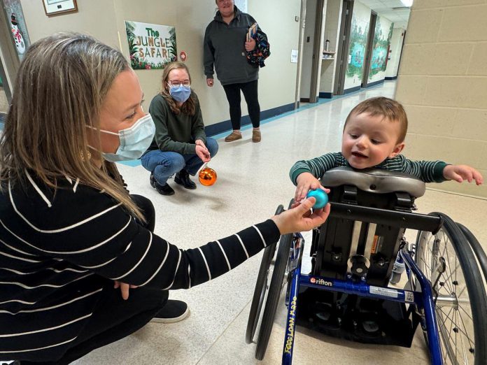 Five Counties Children's Centre occupational therapist Jess hands an ornament to two-year-old Arthur during a recent treatment session. With the help of Five Counties staff, Arthur has taken a significant course correction after a rare form of childhood cancer left him paralyzed from the waist down, including with a mini stand-up wheelchair known as a mobile stander. (Photo courtesy of Five Counties Children's Centre)