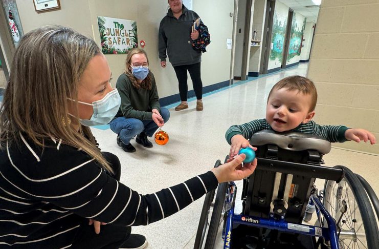 Five Counties Children's Centre occupational therapist Jess hands an ornament to two-year-old Arthur during a recent treatment session. With the help of Five Counties staff, Arthur has taken a significant course correction after a rare form of childhood cancer left him paralyzed from the waist down, including with a mini stand-up wheelchair known as a mobile stander. (Photo courtesy of Five Counties Children's Centre)