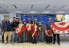 Rashid Sheikh Hassan (fourth from left, with Canadian flag) hugging his mother with his two sisters (wrapped in Canadian flags), brother (third from right, squatting), and father (far right) at Toronto's Pearson International Airport on April 24, 2026, pictured with members of the Azadi Peterborough group that sponsored the Hassan family to come to Canada and join their son in Peterborough. (Photo courtesy of Dave McNab)