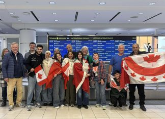 Rashid Sheikh Hassan (fourth from left, with Canadian flag) hugging his mother with his two sisters (wrapped in Canadian flags), his brother (third from right, squatting), and his father (far right) at Toronto's Pearson International Airport on April 24, 2026, pictured with some of the members of the Azadi Peterborough group that sponsored the Hassan family to come to Canada and join their son in Peterborough, including (left to right) Lisa Lowe, Don Park, Matt Park, Brenda Wierdsma-Ibey, Clayton Ibey, Simal Iftikhar, Kristy Hiltz, Karina Bates, and Dave McNab. (Photo courtesy of Dave McNab)