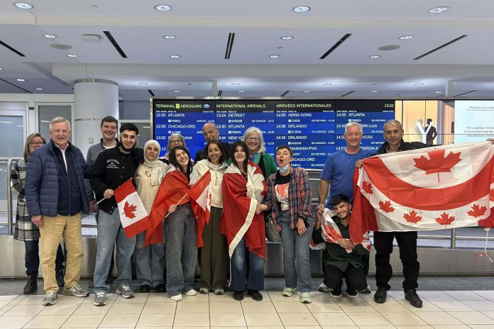 Rashid Sheikh Hassan (fourth from left, with Canadian flag) hugging his mother with his two sisters (wrapped in Canadian flags), his brother (third from right, squatting), and his father (far right) at Toronto's Pearson International Airport on April 24, 2026, pictured with some of the members of the Azadi Peterborough group that sponsored the Hassan family to come to Canada and join their son in Peterborough, including (left to right) Lisa Lowe, Don Park, Matt Park, Brenda Wierdsma-Ibey, Clayton Ibey, Simal Iftikhar, Kristy Hiltz, Karina Bates, and Dave McNab. (Photo courtesy of Dave McNab)