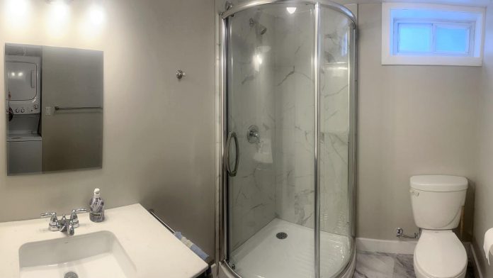 The bathroom of a self-contained basement apartment at a residential property owned by One City Peterborough, part of a partnership with Peterborough Action for Tiny Homes to construct additional rental units (ARUs). Reflected in the mirror is a washer-dryer unit. (Photo: Mackenzie Clark-Smith / One City Peterborough)
