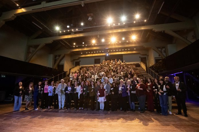 Speakers and the audience at the "A Conversation About The Status of Women In Our Community" event at Market Hall in downtown Peterborough on March 31, 2026, presented by Maryam Monsef's organization ONWARD in partnership with the Peterborough and Kawarthas Chamber of Commerce. Everyone received a white rose in the memory of the late Peterborough civic leader Ann Farquharson, who died unexpectedly in late 2025 and in whose honour the event was held. (Photo: Jordan Lyall / kawarthaNOW)