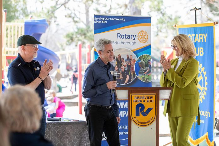 Rotary Club of Peterborough president Tony Grady (middle) announcing that $288,250 has been raised for the new Rotary Accessible Playground to date as steering committee chair Betty Halman-Plumley applauds during an event at the Riverview Park and Zoo on April 22, 2026. (Photo: Jordan Lyall / kawarthaNOW)