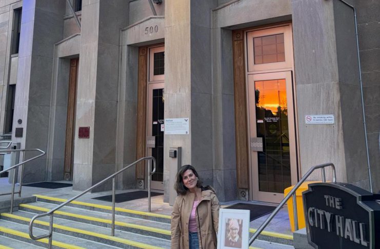 Peterborough resident Brooke Roberts holding a photo of her late daughter Sofie while standing outside Peterborough City Hall on May 2, 2026, when it was lit up in grey, yellow, and teal in honour of Brain Cancer Awareness Month. Brooke is an ambassador for Brain Cancer Canada, a national charity that works to raise awareness and bridge the gap in funding for brain cancer research and access. (Photo courtesy of the Roberts family)