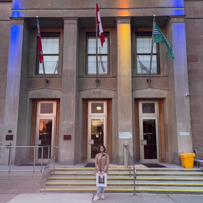 Peterborough resident Brooke Roberts holding a photo of her late daughter Sofie while standing outside Peterborough City Hall on May 2, 2026, when it was lit up in grey, yellow, and teal in honour of Brain Cancer Awareness Month. Brooke is an ambassador for Brain Cancer Canada, a national charity that works to raise awareness and bridge the gap in funding for brain cancer research and access. (Photo courtesy of the Roberts family)