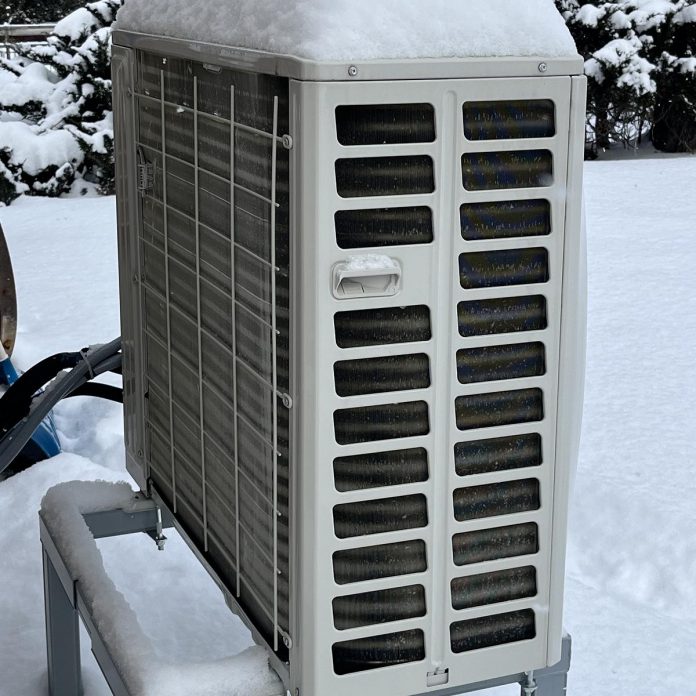 Heat pumps are proven technology that work well even on the coldest winter days. This view of the back side of a heat pump shows the refrigerant coils, as well as the importance of installing the outdoor unit on a stand to keep it above the level of the snow. (Photo: Bryn Magee / GreenUP)