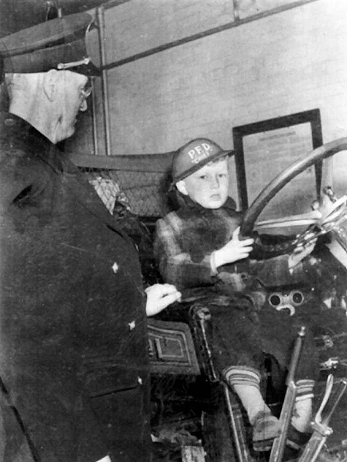 James Clarke sitting behind the wheel of a firetruck as a young child. His tumultuous childhood growing up in Peterborough during the Second World War is the subject of his 2012 memoir "The Kid from Simcoe Street," which has been adapted for the stage by Trent Valley Archives Theatre. Ahead of the performances from June 4 to 7, 2026, audiences can get a walking tour of "The World of the Kid on Simcoe Street" presented by Trent Valley Archives on May 24 and 31. (Photo courtesy of the Clarke family)