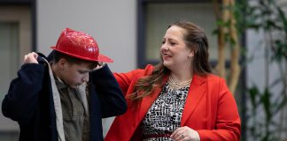 Charlie Harris as young Jimmy Clarke with Lauren Murphy as his mother Florie Clarke during a special preview dress rehearsal of Trent Valley Archives Theatre's "The Kid from Simcoe Street" at Canterbury Gardens in Peterborough on May 28, 2026. In this scene, Jimmy is putting on firefighter gear he received from the brigade at Fire Hall No. 1 when they made him their fire mascot as a reward for calling in a chimney fire. Based on the memoir of retired Ontario Superior Court Justice and poet James Clarke, who grew up on Simcoe Street in downtown Peterborough, the play runs for four performances at Market Hall Performing Arts Centre from Thursday, June 4 until Sunday, June 7. (Photo: Jordan Lyall Photography)