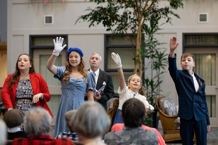 The Clarke family, played (from left to right) by Lauren Murphy, Lily Faulkner, Trudy Conroy, and Charlie Harris, during a special preview dress rehearsal of Trent Valley Archives Theatre's "The Kid from Simcoe Street" at Canterbury Gardens in Peterborough on May 28, 2026. In this scene, the family is waving goodbye to patriarch Sam (Ron Jewer, not pictured) as he departs the Peterborough CPR station with other recruits to fight in the Second World War. In the background, narrator Jim Mills tells the story of the Clarke family. (Photo: Jordan Lyall Photography)