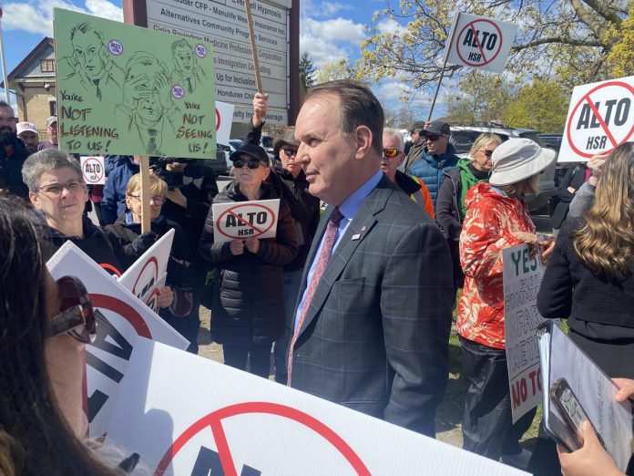 Federal transport minister Steven MacKinnon wades into a crowd of people protesting against the Alto high-speed rail project outside the office of the Peterborough and Kawarthas Chamber of Commerce after he arrived to speak at an event hosted by the Chamber on May 8, 2026. (Photo: Paul Rellinger / kawarthaNOW)