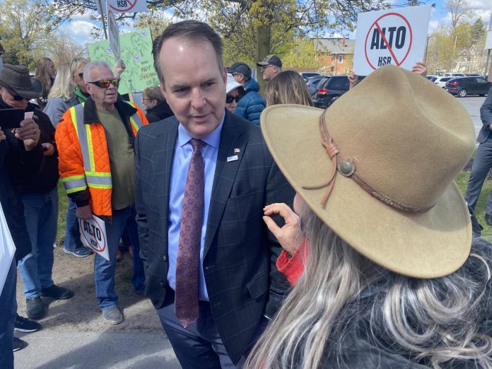 Federal transport minister Steven MacKinnon listens to a woman who was part of a crowd of people protesting against the Alto high-speed rail project outside the office of the Peterborough and Kawarthas Chamber of Commerce after he arrived to speak at an event hosted by the Chamber on May 8, 2026. (Photo: Paul Rellinger / kawarthaNOW)