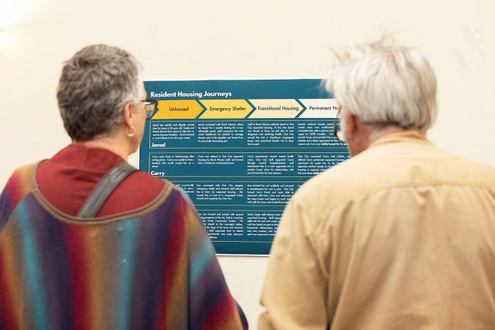 Attendees during an event to discuss One City Peterborough's housing strategy at Knights of Columbus Hall on May 12, 2026 read a poster describing the journeys of people who have moved from being unhoused through the housing continuum of emergency shelter, transitional housing, and permanent housing.(Photo: Jordan Lyall / kawarthaNOW)
