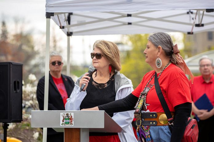 Hiawatha First Nation Chief Laurie Carr speaks during an event to commemorate Red Dress Day at Peterborough City Hall on May 5, 2026, with Curve Lake First Nation's Shelley Knott, Indigenous relations advisor for the City of Peterborough, by her side. Pictured in the background are Peterborough city councillor Joy Lachica and Peterborough mayor Jeff Leal. (Photo: Jordan Lyall / kawarthaNOW)