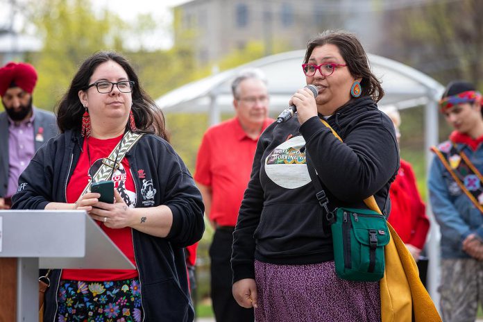 Em Feltham Day and Jess Vossen of the Urban Indigenous Working Group during an event to commemorate Red Dress Day at Peterborough City Hall on May 5, 2026. Pictured in the background are City of Peterborough CAO Jasbir Raina, Peterborough mayor Jeff Leal, Peterborough County warden Bonnie Clark (obscured), and Kelvin Boissoneau of Garden River First Nation. (Photo: Jordan Lyall / kawarthaNOW)