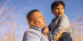 An Indigenous man holding a boy in his arms with a field in the background. (Photo: Alto)