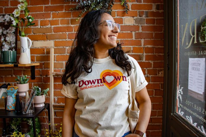 Nour Mazloum, who is celebrating two years as executive director of the Peterborough Downtown Business Improvement Area (DBIA), models a T-shirt branded with the original "The Heart of It All" logo from when the organization was founded in 1981. In honour of its 45th anniversary, the DBIA will be rolling out the retro logo on T-shirts and related merchandise. (Photo courtesy of Peterborough DBIA)